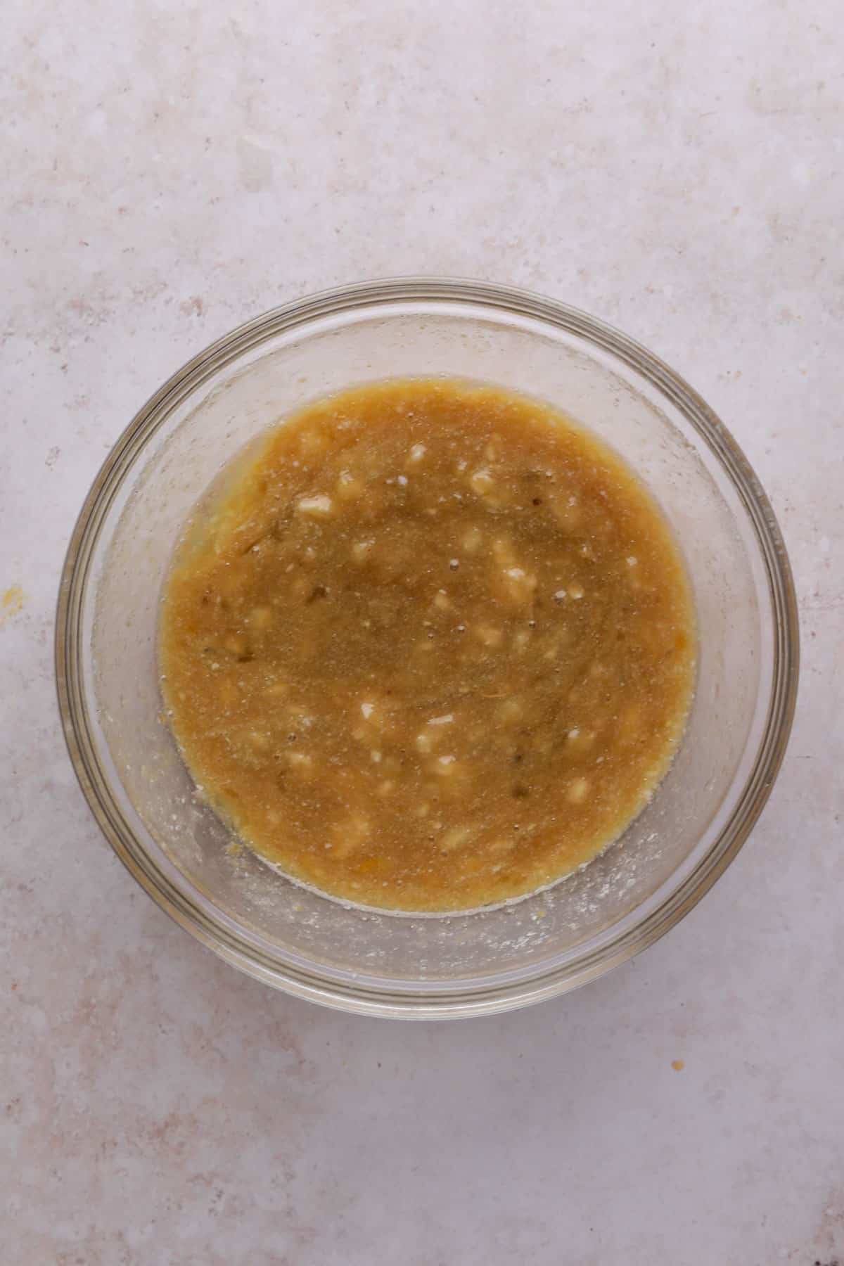 Whisked wet ingredients for banana donuts in a glass mixing bowl.