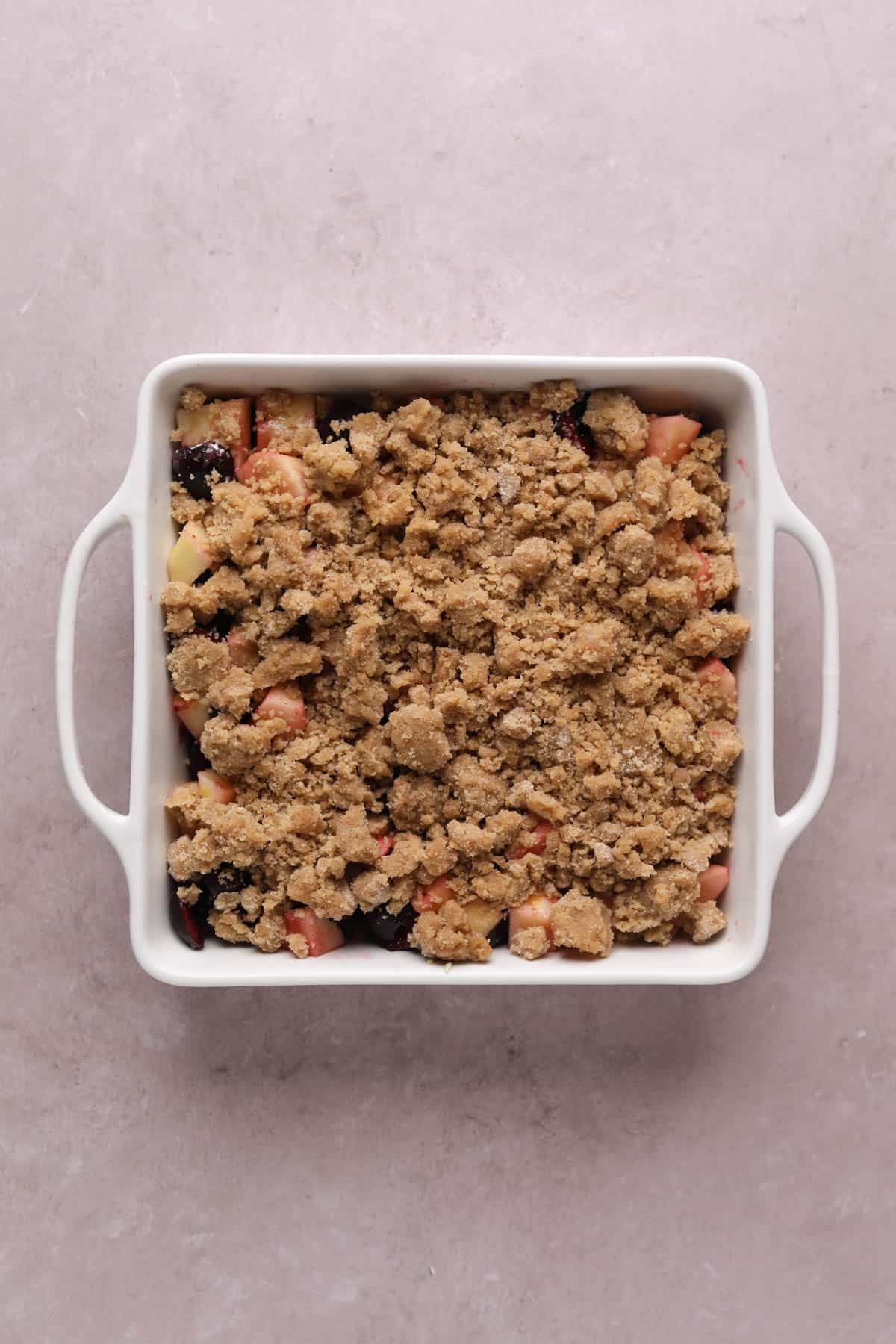 Unbaked cherry apple crumble in a white ceramic baking dish.