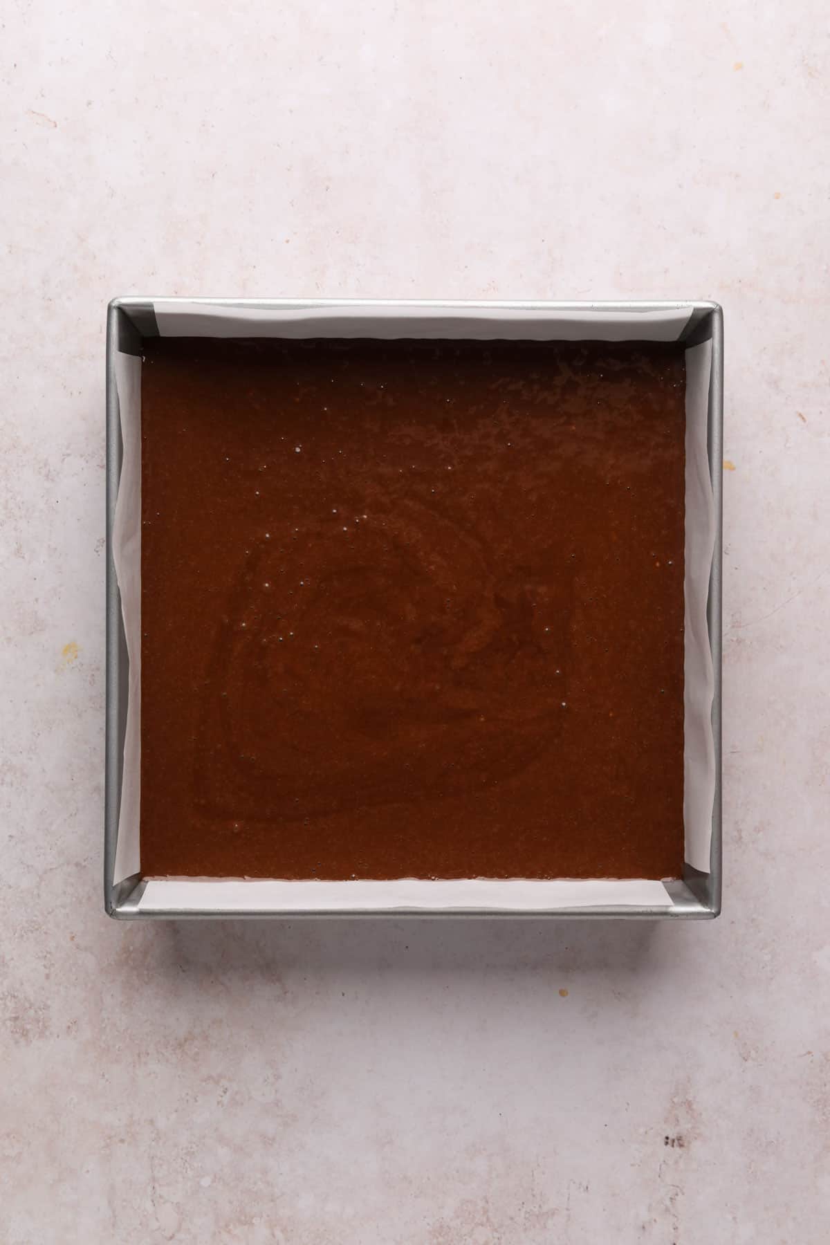 Chocolate fudge cake batter in a 9x9 square baking pan lined with parchment paper.