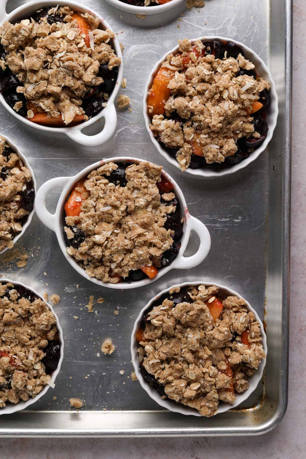 Unbaked peach cherry crisps in ramekins on a baking sheet.