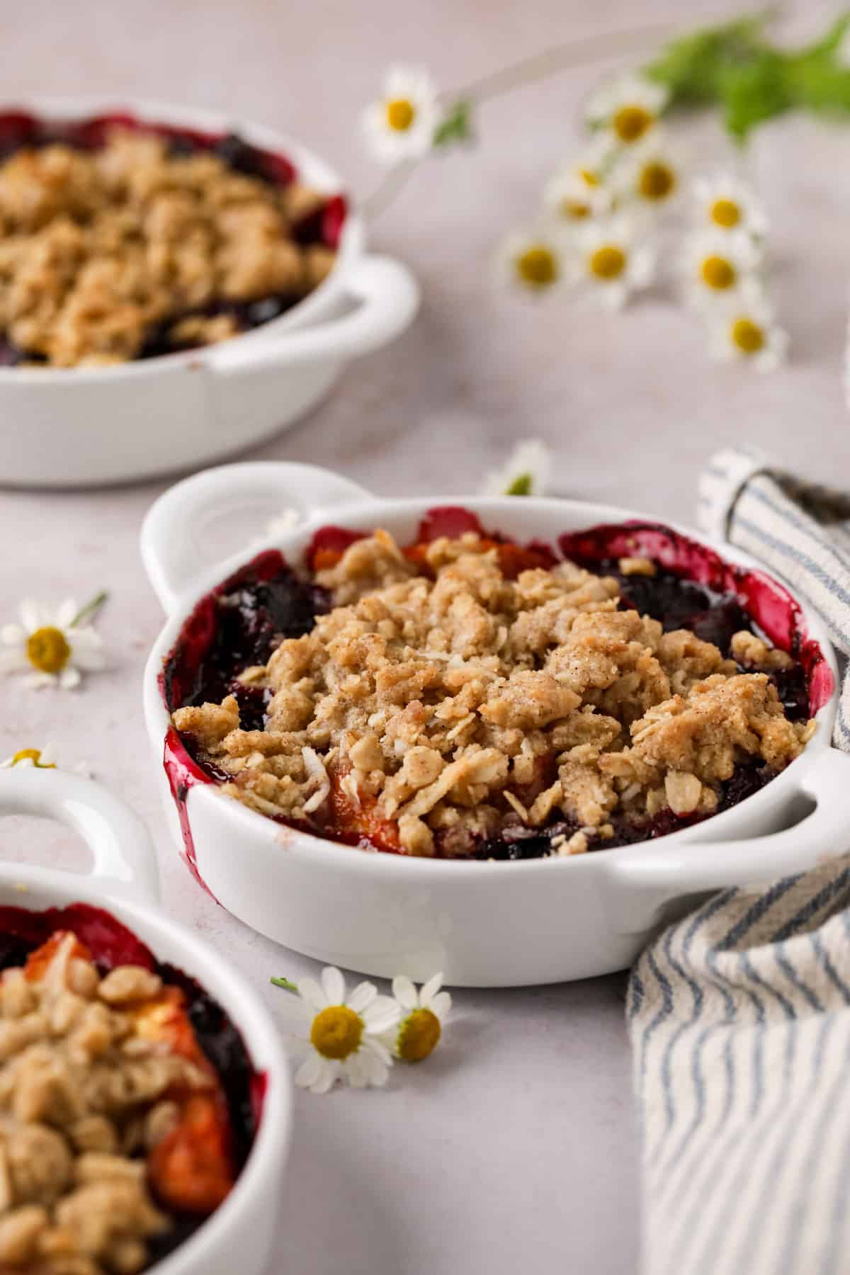 Individual peach cherry crisps baked in white handled ramekins with an oat crumble topping.