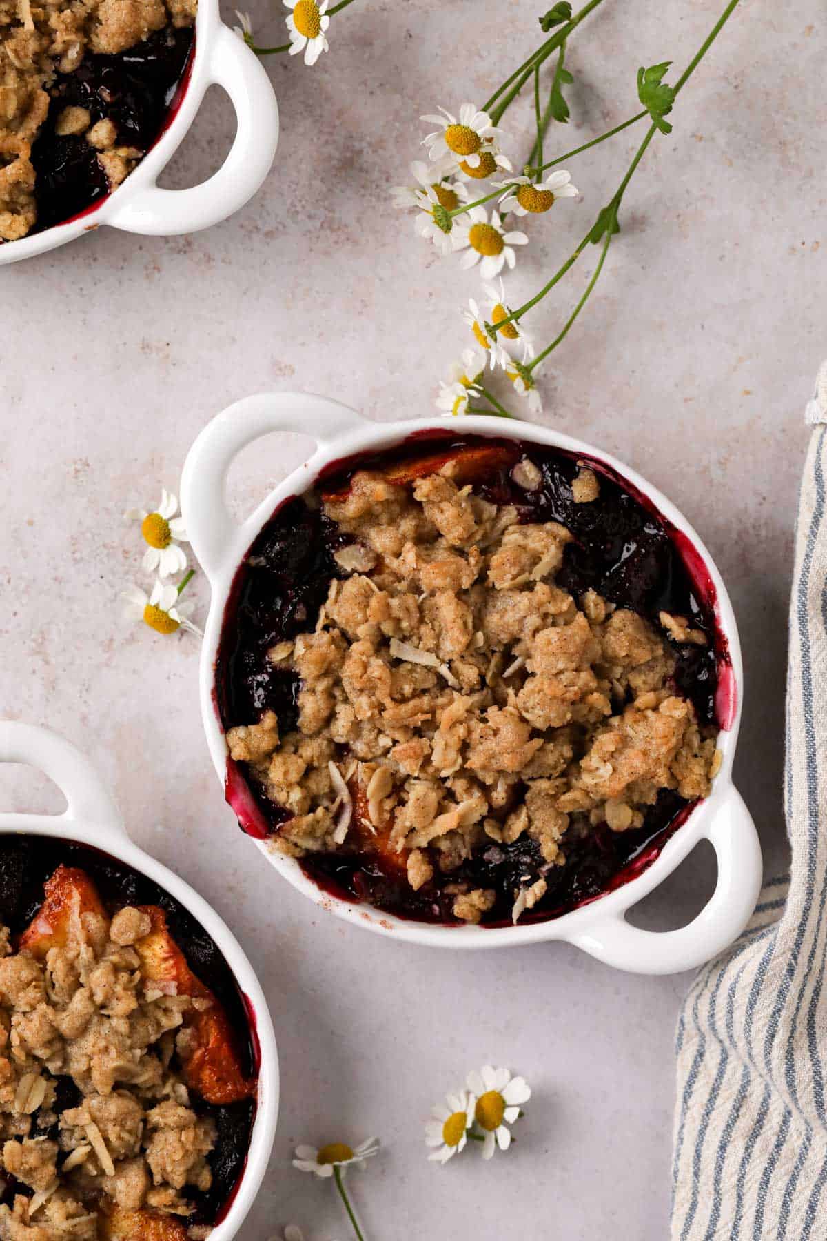 Overhead shot of individual peach cherry crisps baked in white handled ramekins with an oat crumble topping.