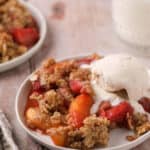 Two white dishes with strawberry peach crisp and a scoop of vanilla ice cream.