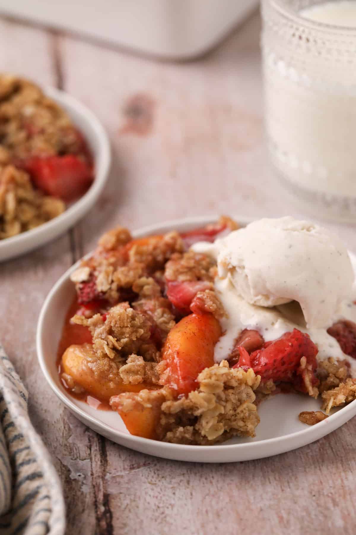 Two white dishes with strawberry peach crisp and a scoop of vanilla ice cream.