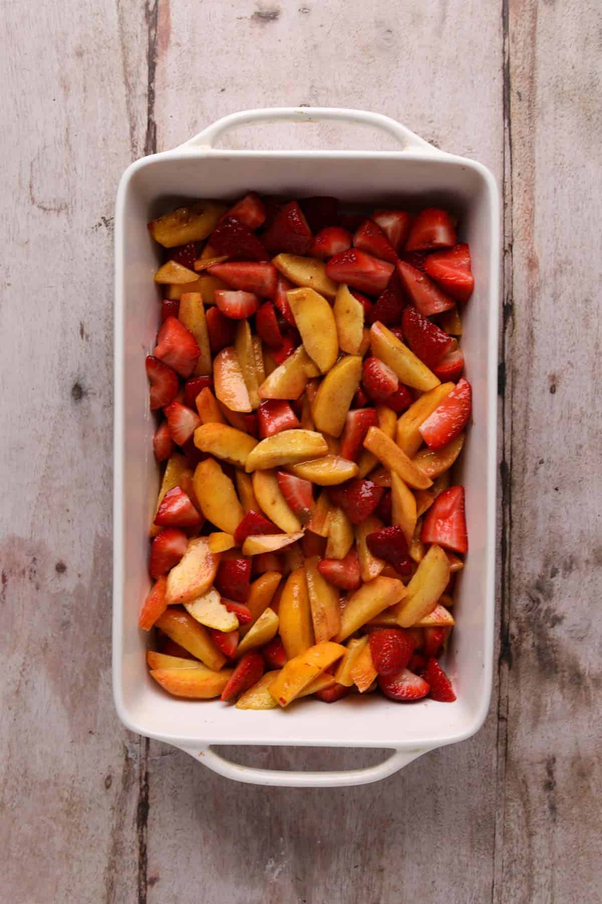 Strawberry peach filling spread in an even layer in a white ceramic 8x11 baking dish.