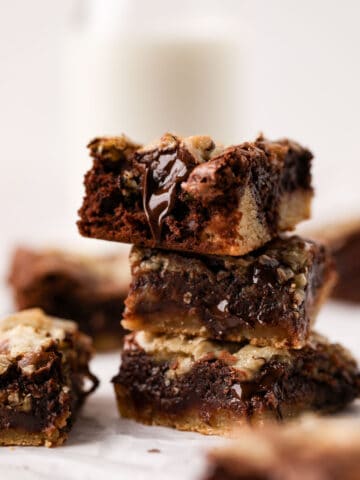 Stack of three brownie blondie squares on a flat surface with parchment paper.