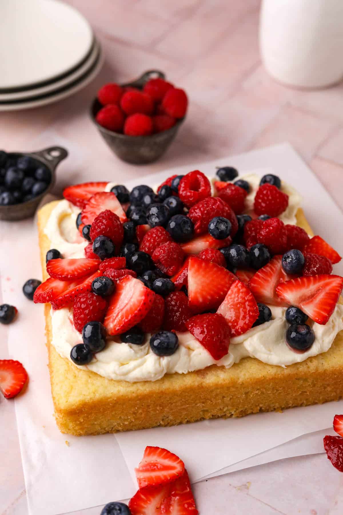 One layer, square lemon berry mascarpone cake with mascarpone frosting and macerated berries on a flat surface with parchment paper.