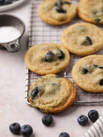 Lemon blueberry cookies on a wire cooling rack with blueberries and salt in containers.