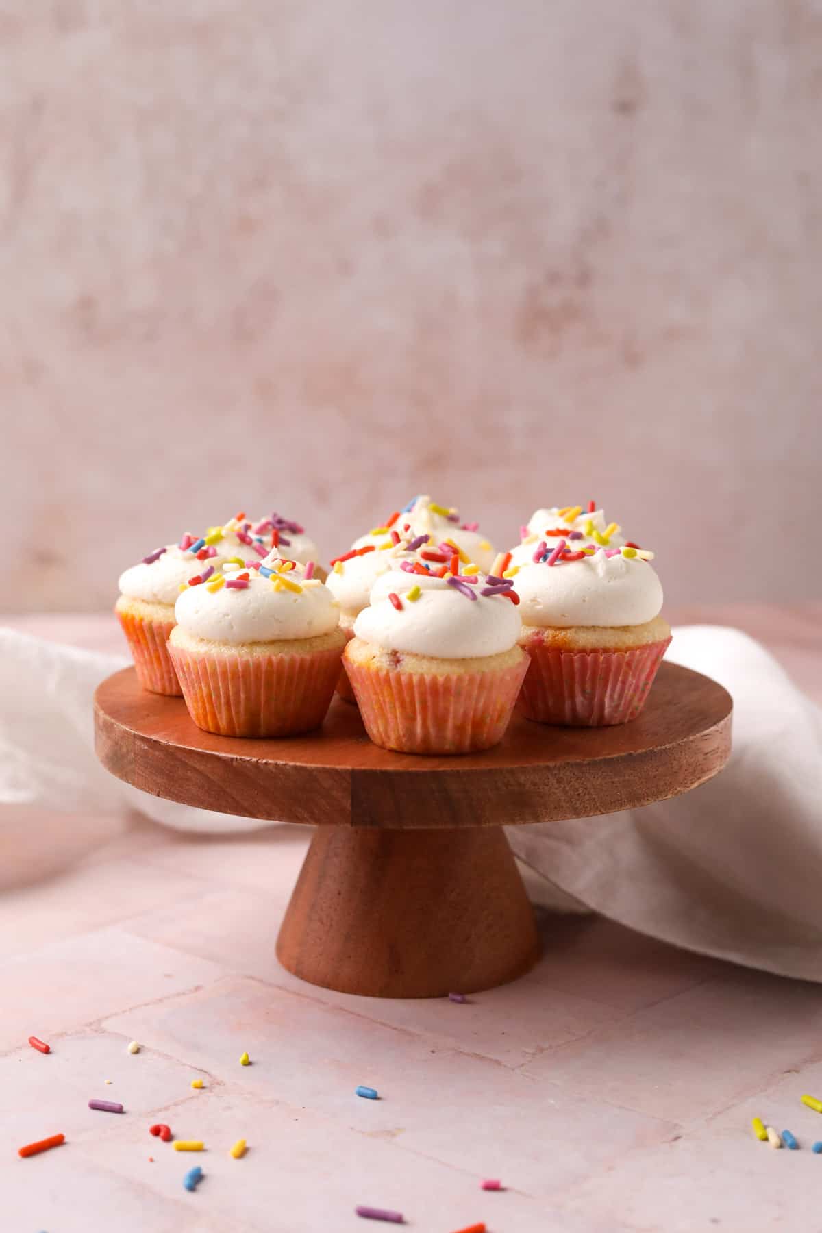 Mini funfetti cupcakes with vanilla buttercream and sprinkles on a wood cake stand.