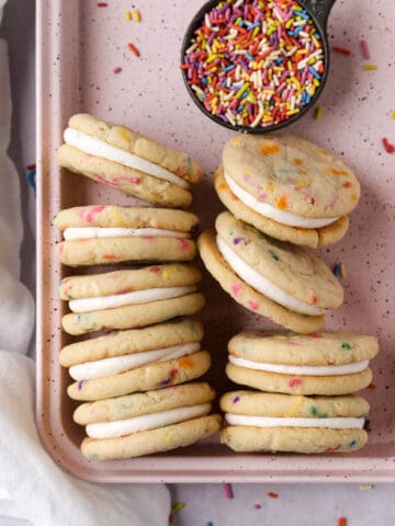 Overhead shot of funfetti cookie sandwiches stacked on their sides in a pink baking pan with sprinkles.