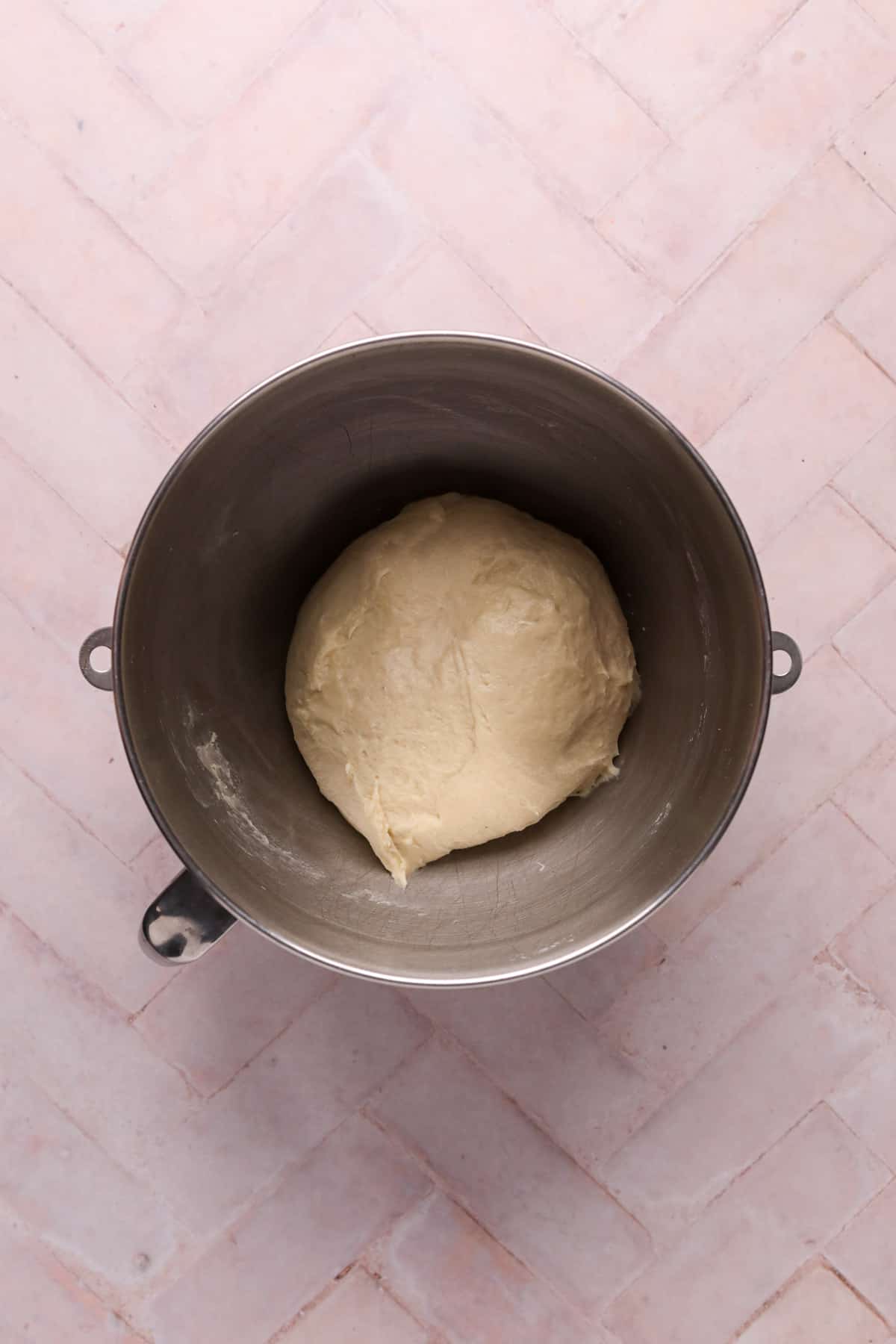 Mixed cinnamon roll dough in a metal stand mixer bowl on a flat surface.