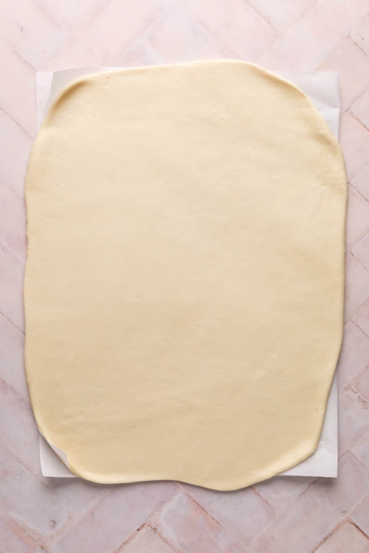 Cinnamon roll dough rolled into a large rectangle on parchment paper set on a flat surface.