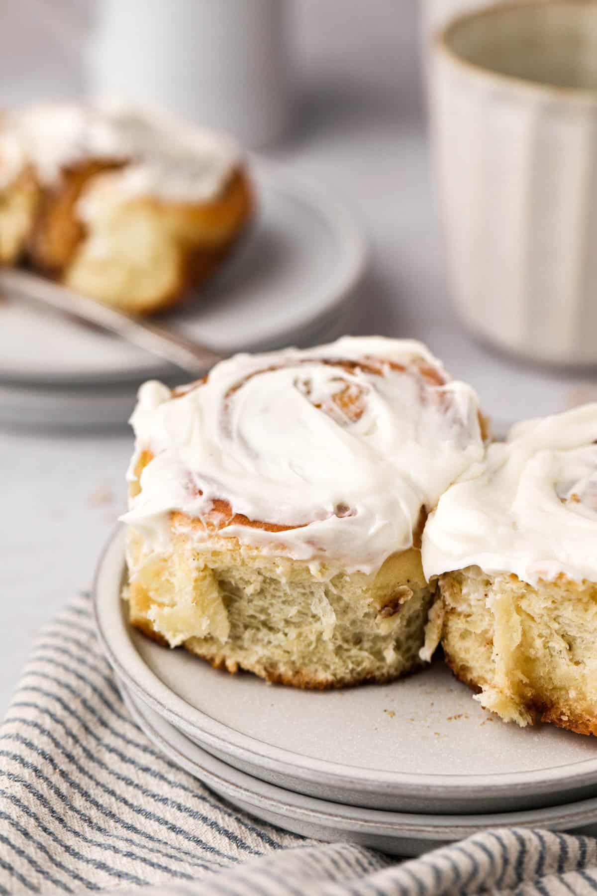Close up of two homemade soft and fluffy cinnamon rolls with cream cheese frosting set in plate.