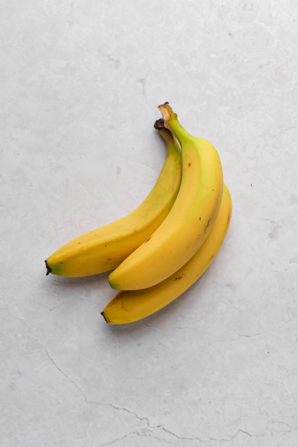 Bunch of three bananas on a flat surface.