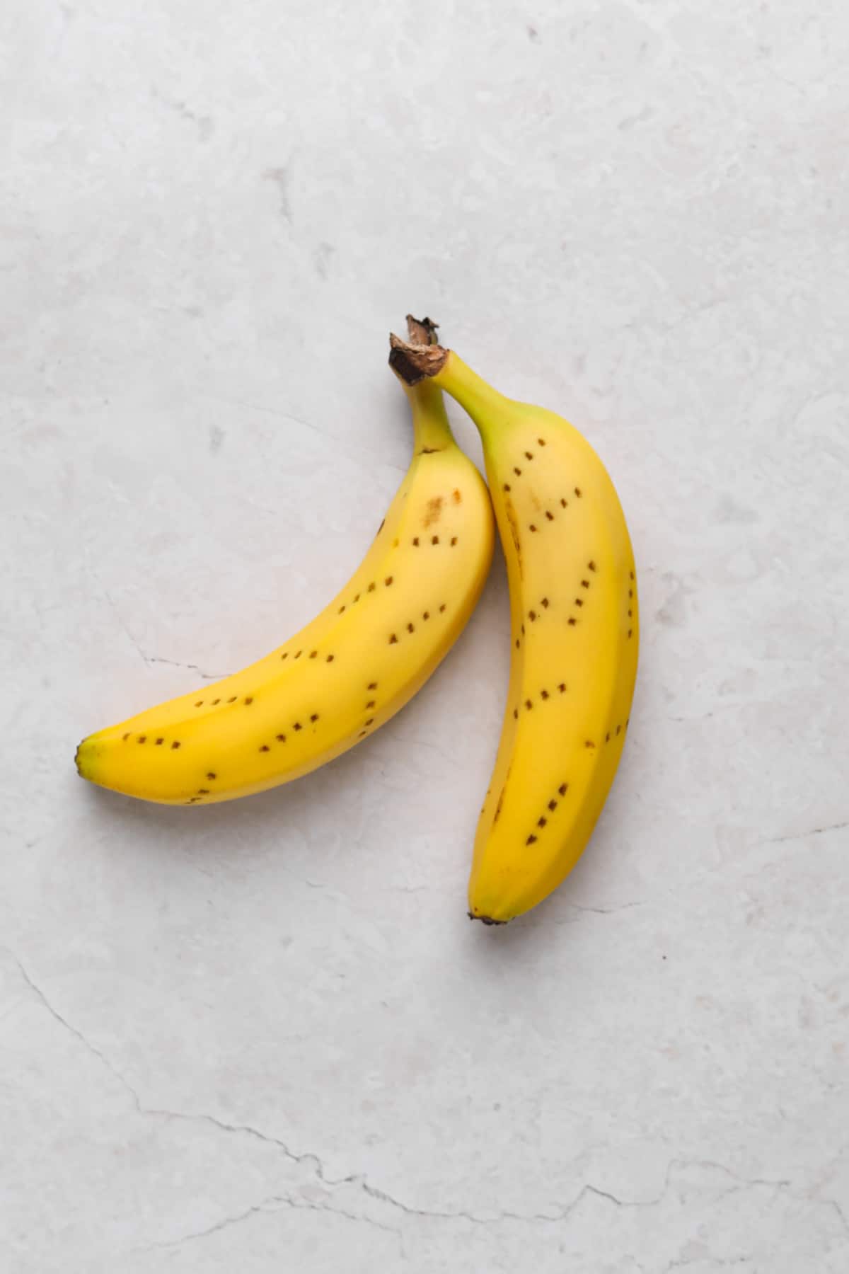 Two yellow bananas on a flat surface with pricked fork holes all over.