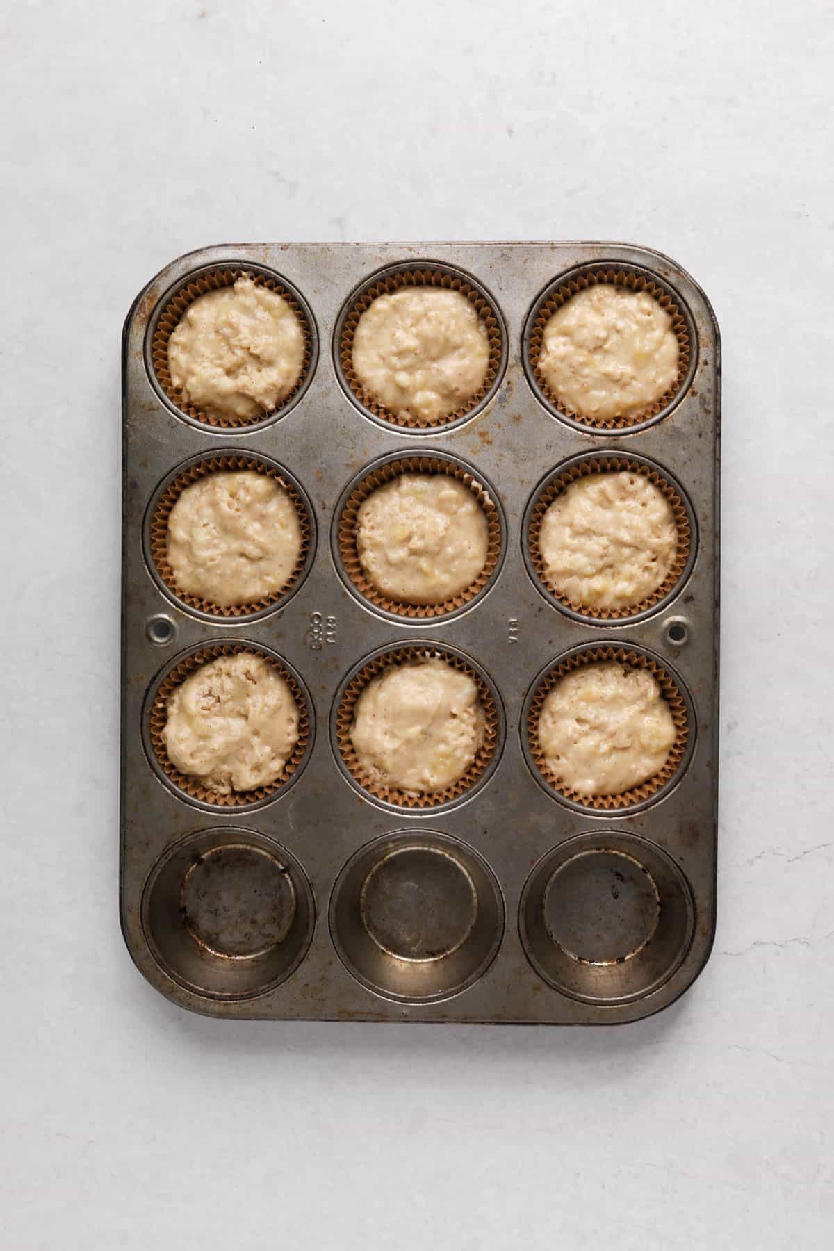 Sour cream banana muffin batter divided into 9 muffins in a metal muffin pan.