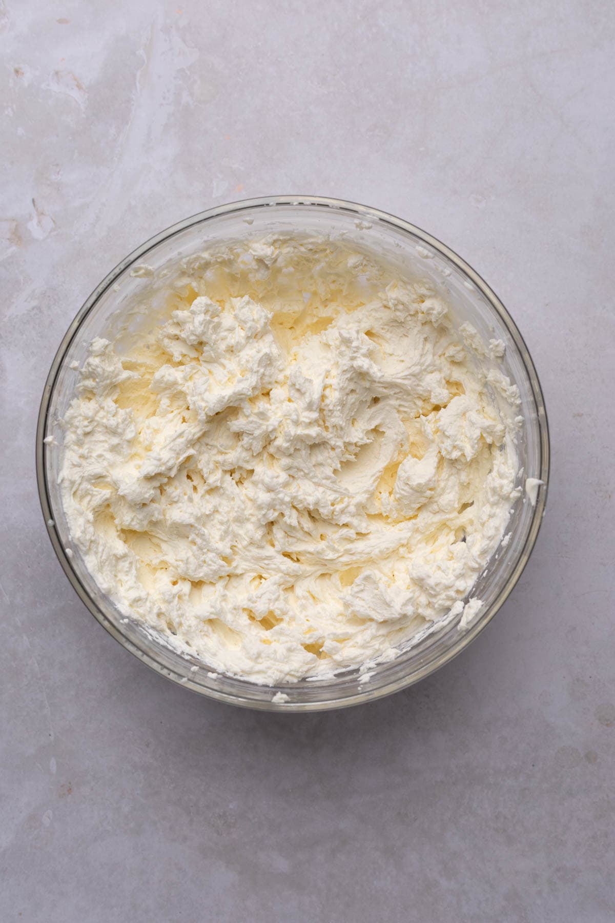 Heavy cream, sugar, and mascarpone cheese whisked to stiff peaks in a glass bowl.