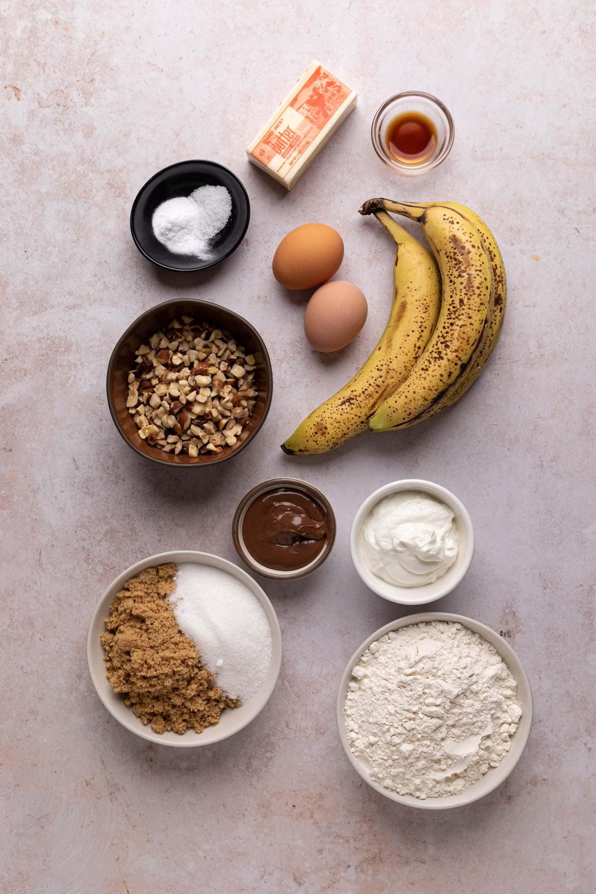 Ingredients for banana hazelnut bread in bowls on a flat surface.