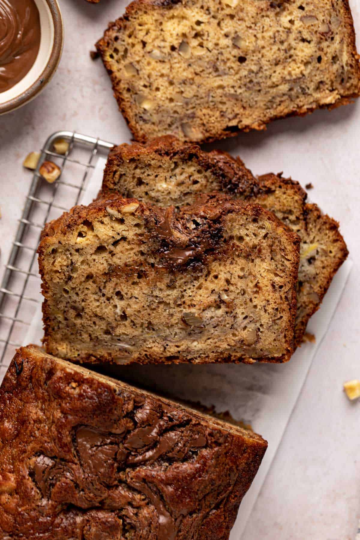 Overhead close up of slices of banana hazelnut bread on a rectangular metal cooling rack set on a flat surface.