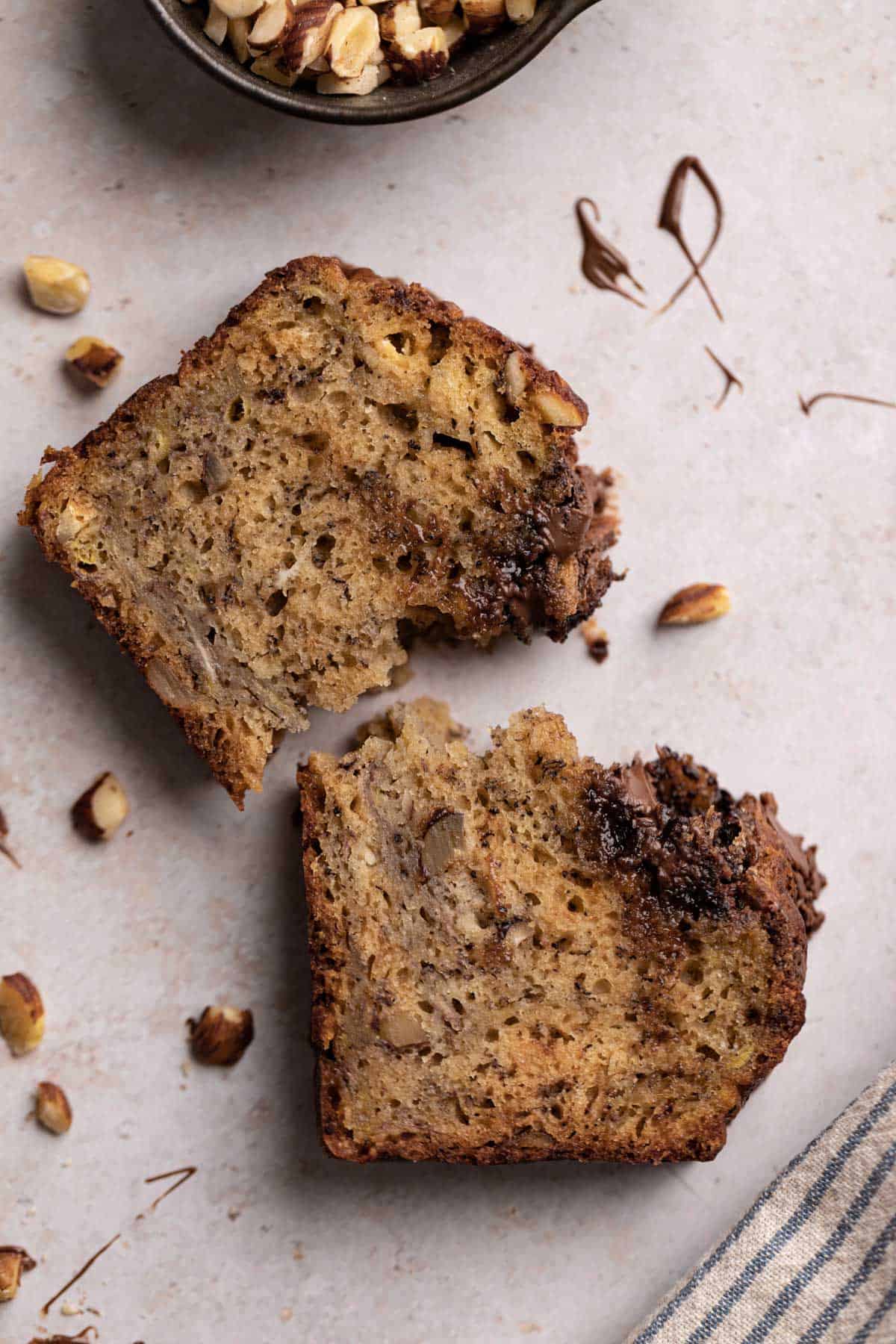 Close up overhead shot of a slice of banana hazelnut bread broken into two pieces set on a flat surface.