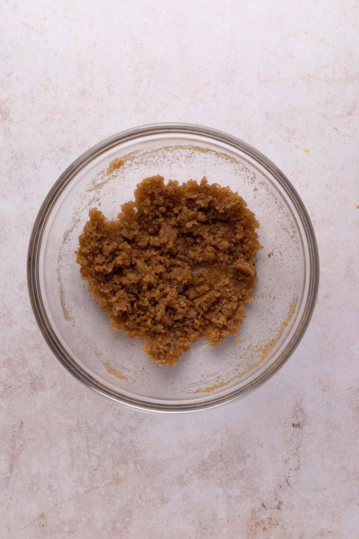 Whisked sugars with browned butter in a glass mixing bowl set on a flat surface.