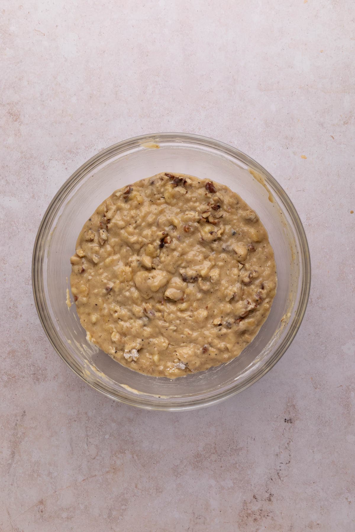 Mixed batter for banana hazelnut bread in a glass mixing bowl set on a flat surface.