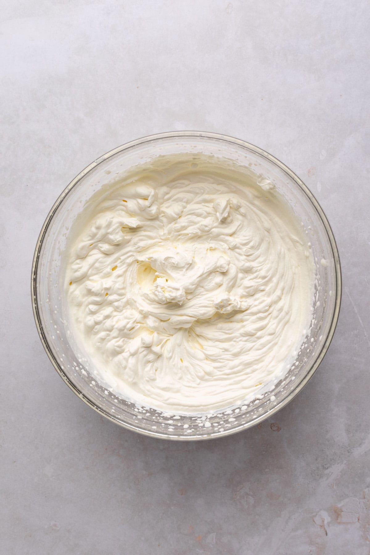 Heavy cream whisked to stiff peaks in a glass bowl on a flat surface.