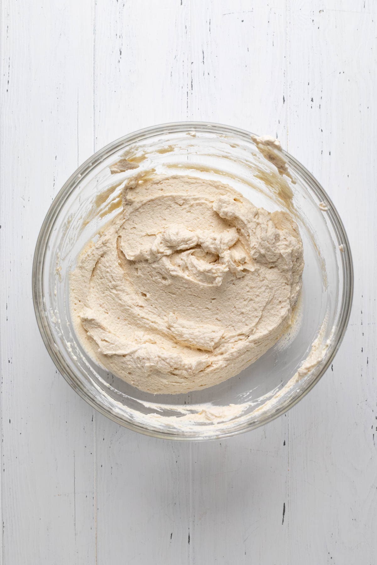 Whipped cream combined with Biscoff spread and mascarpone cheese in a glass mixing bowl.