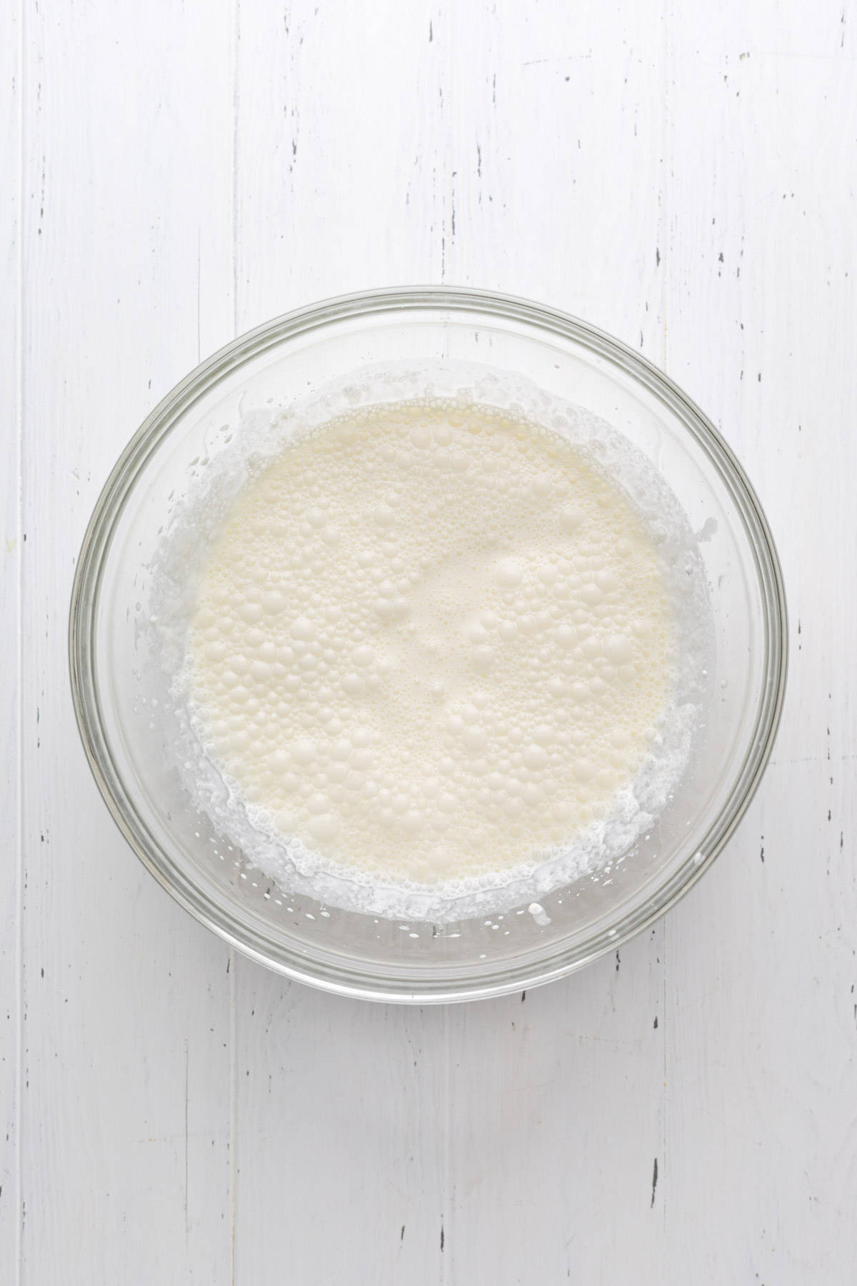 Heavy cream, powdered sugar, and vanilla combined until frothy in a glass mixing bowl.