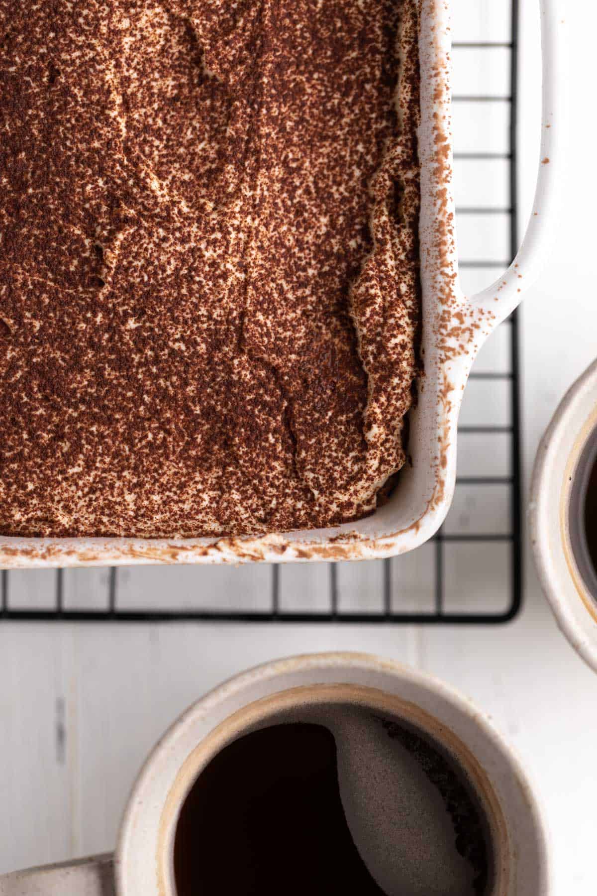 Overhead close up of Biscoff tiramisu in a sqaure white ceramic baking dish with coffee in the background.