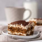 Close shot of a slice of Biscoff tiramisu set on a white round plate and cream linen napkin.