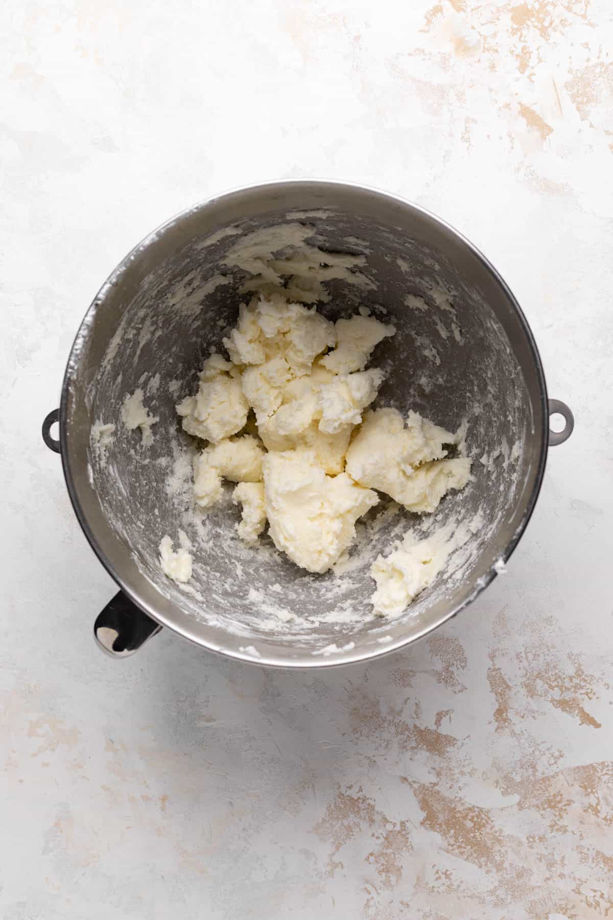 Creamed butter and powdered sugar in a metal stand mixer bowl set on a flat surface.