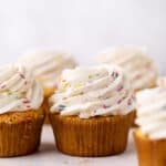 Funfetti buttercream frosting swirled on funfetti cupcakes set on a flat surface.