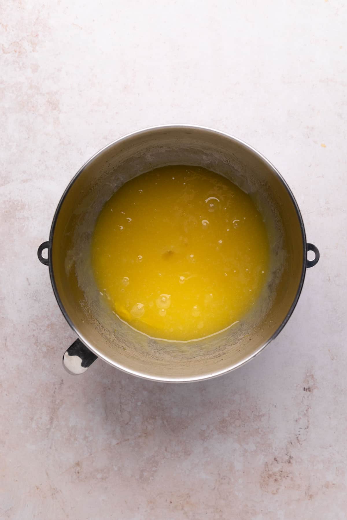 Eggs and vanilla combined with sugar and oil for carrot cake in a metal mixing bowl set on a flat surface.