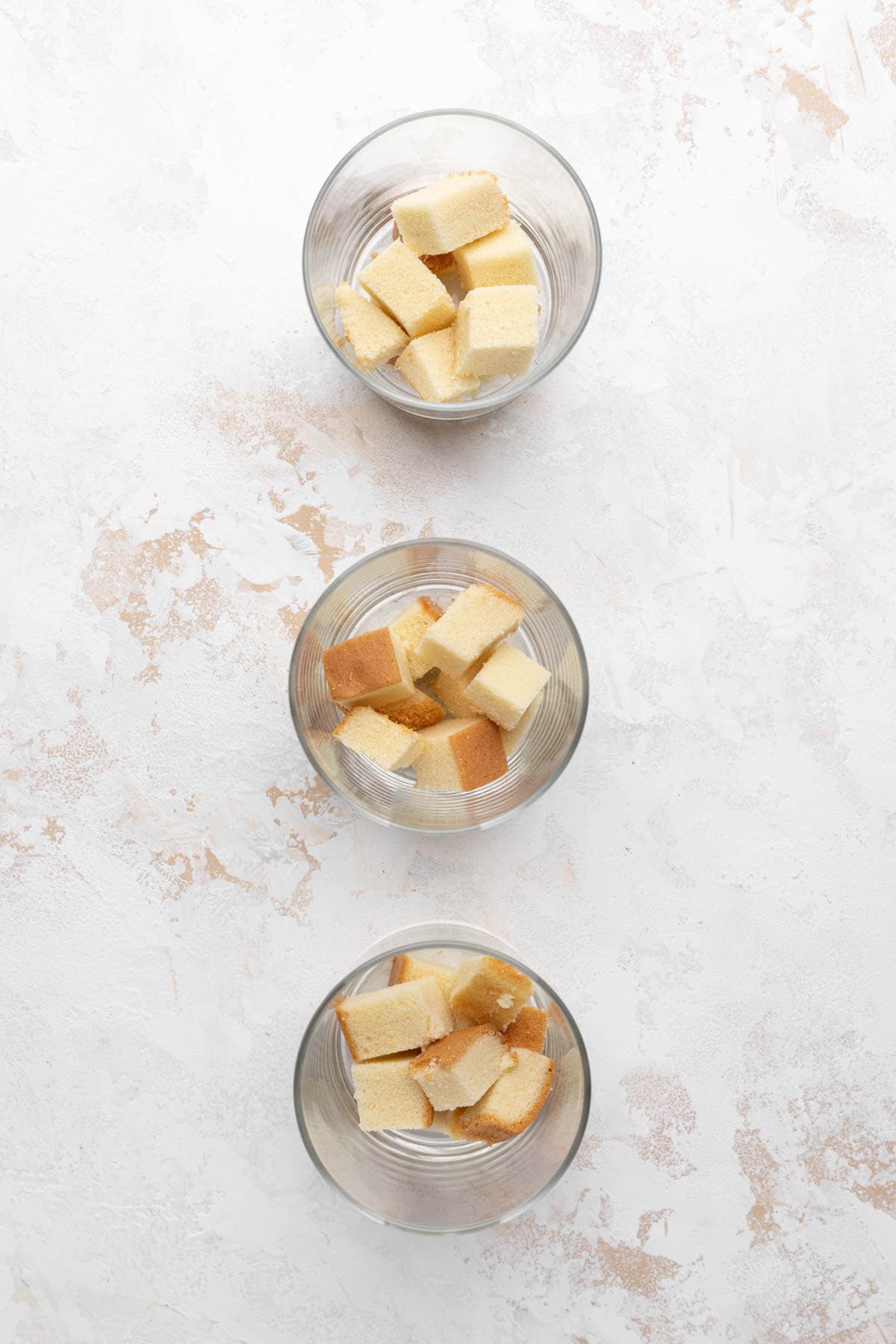 Ovverhead shot of three glasses with a layer of cubed pound cake.