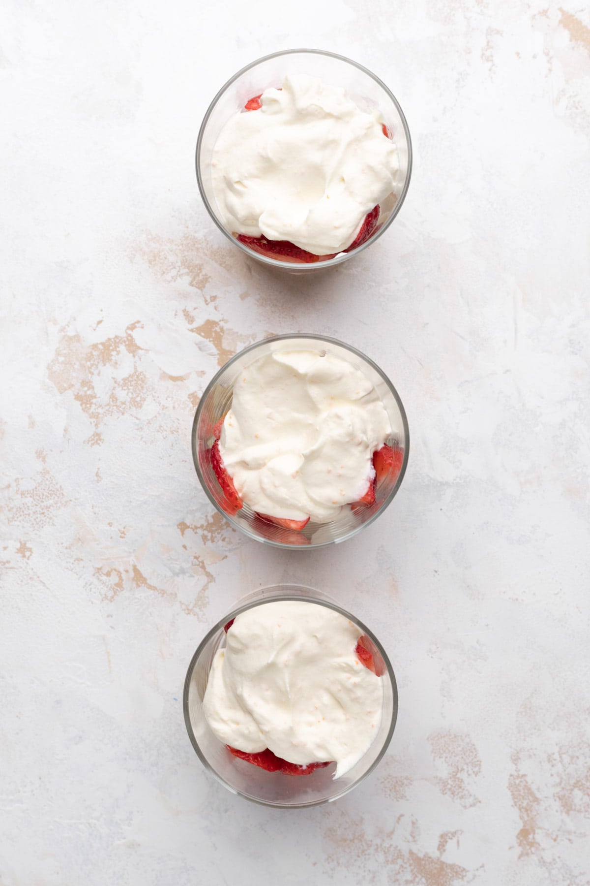 Overhead shot of three glasses with a layer of cubed pound cake, macerated strawberries, and fresh whipped cream.