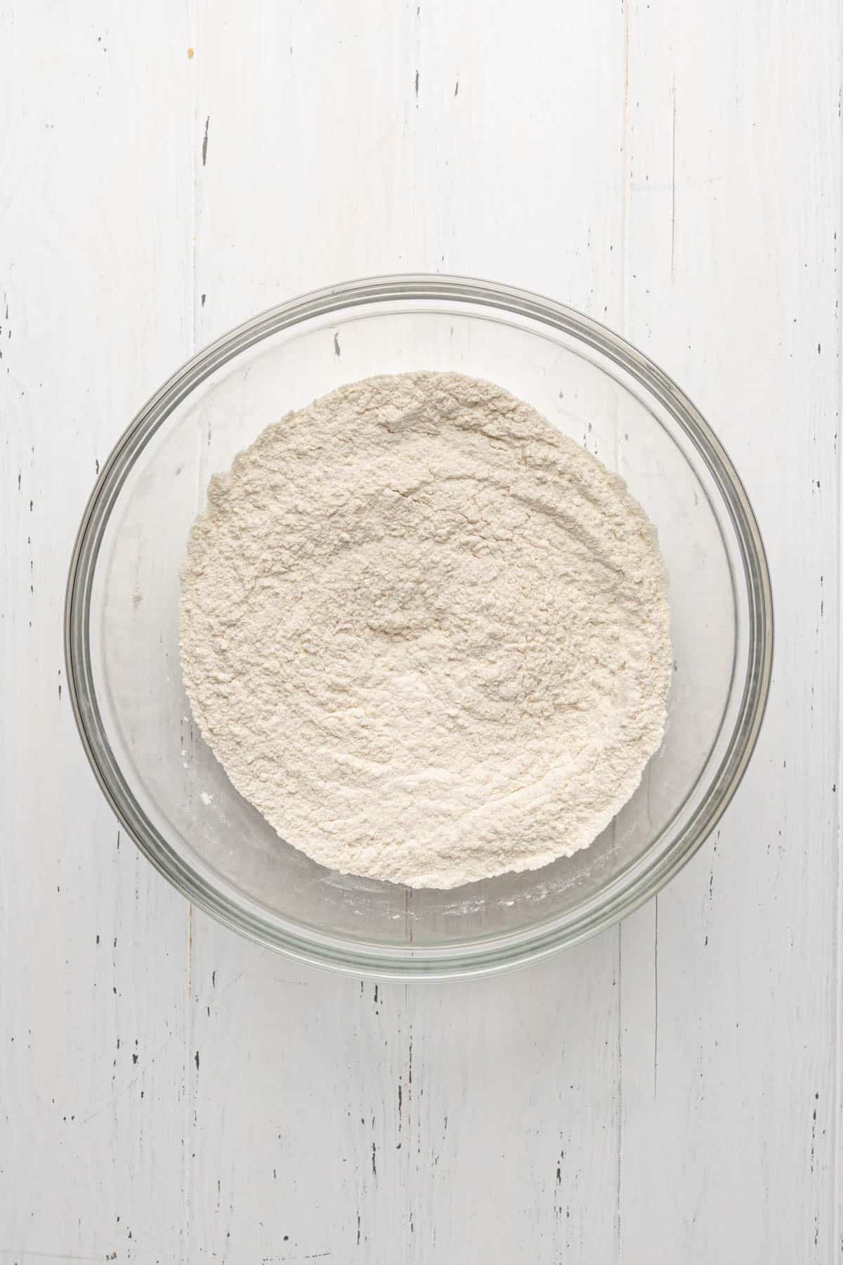 Whisked dry ingredients for pie dough in a glass mixing bowl set on a flat white surface.