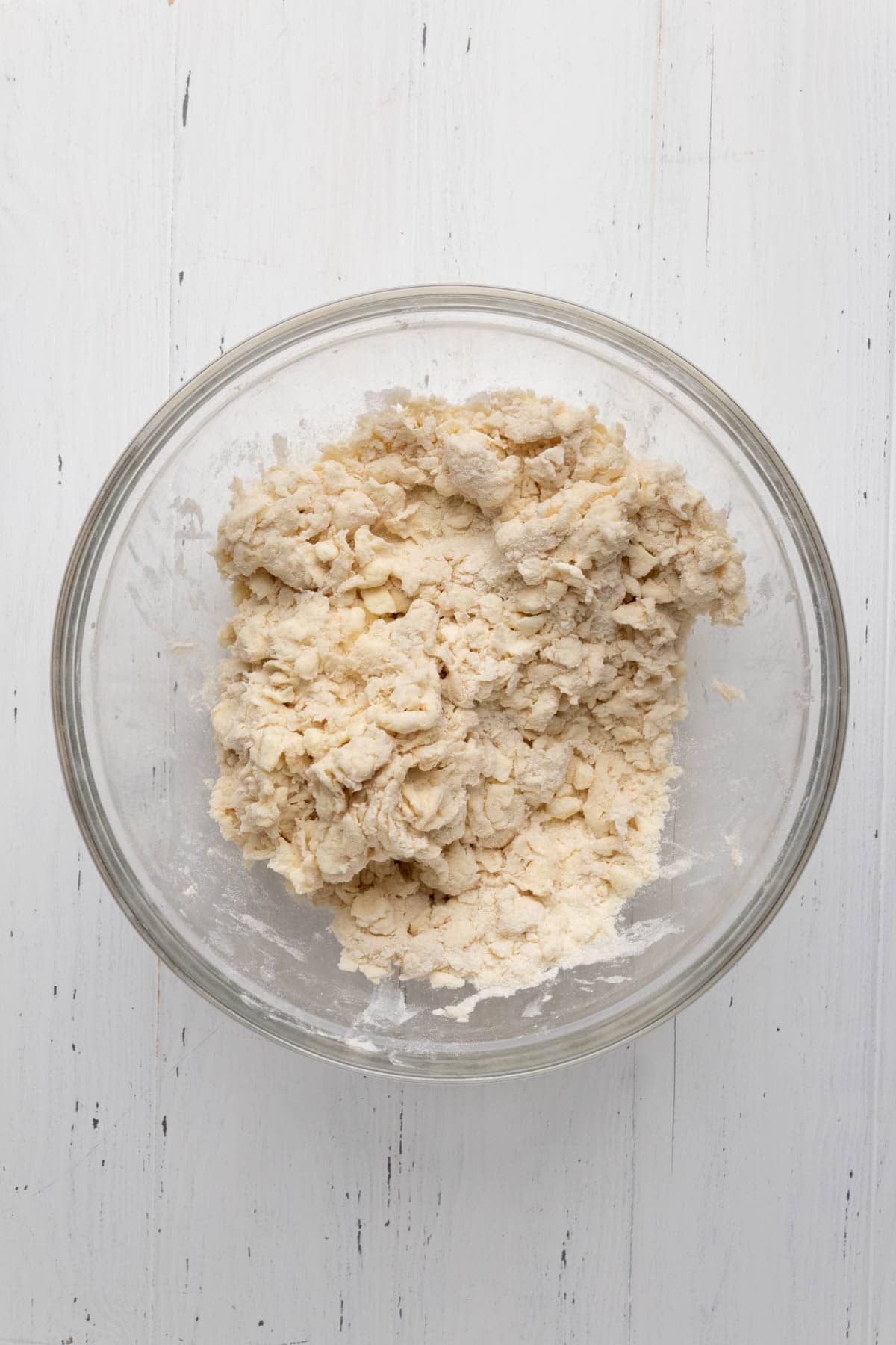 All butter pie dough mixed in a glass mixing bowl set on a flat white surface.