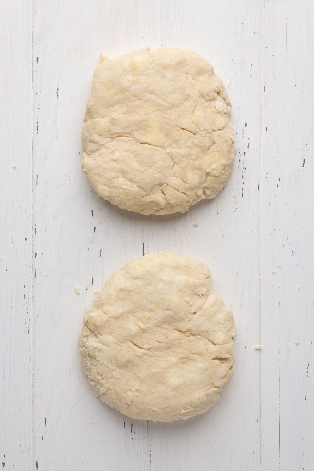 Two round pie crust dough shaped into disc sets on a flat white wood surface.