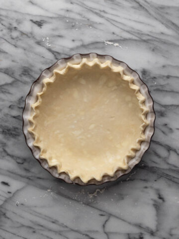 Unbaked fluted all butter pie crust in a pie plate set on a marble stone.