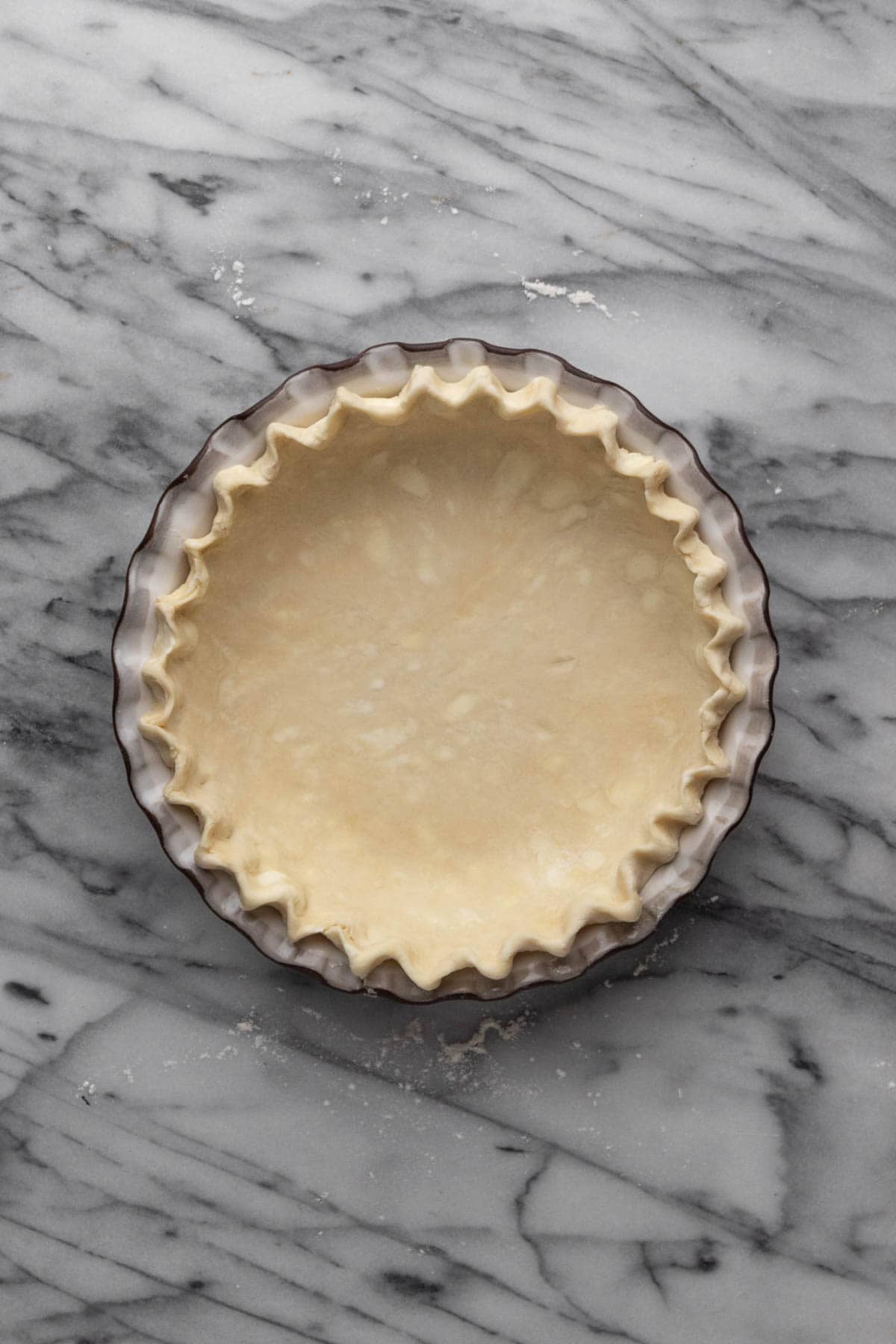 Unbaked fluted all butter pie crust in a pie plate set on a marble stone.