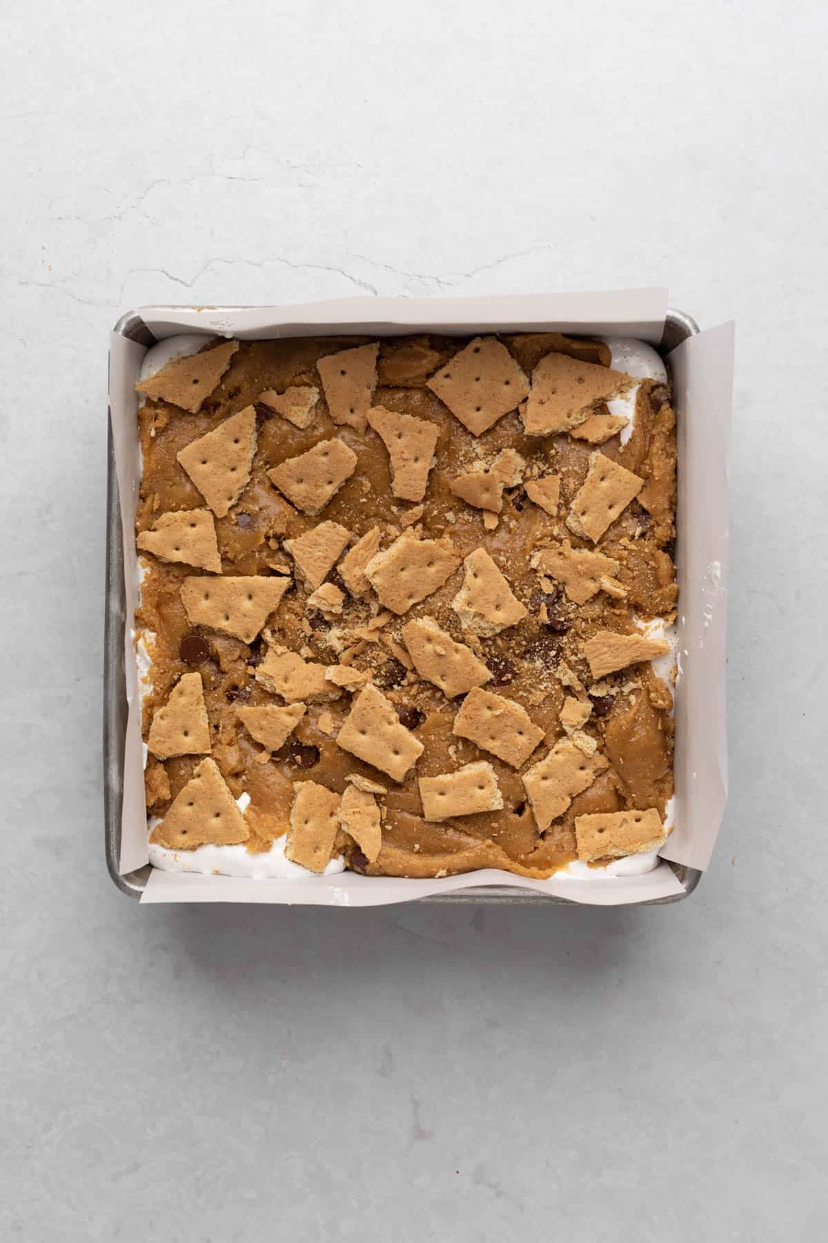 S'more blondies in a square aluminum baking pan lined with parchment paper ready for baking.