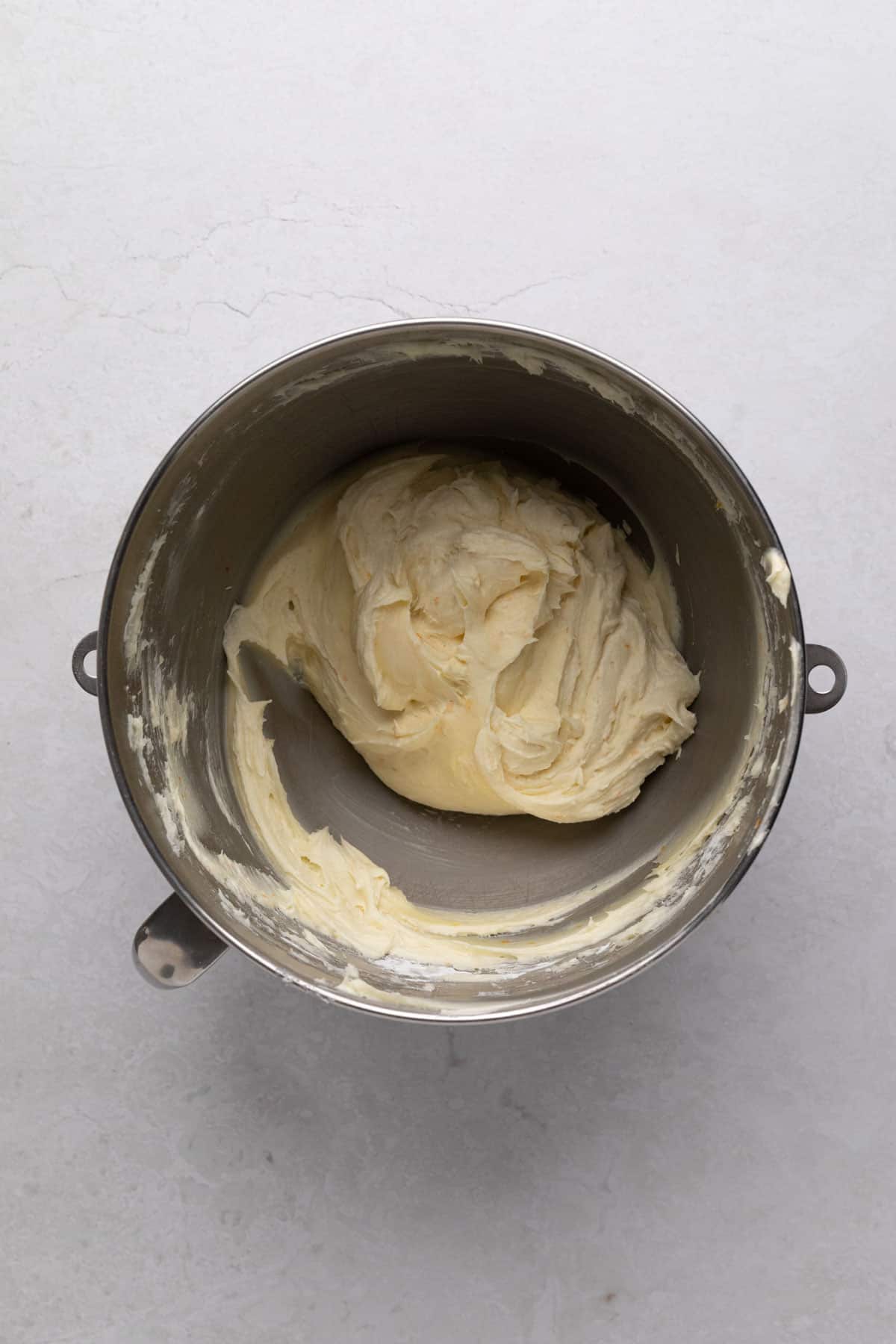 Orange cream cheese frosting mixed in a metal stand mixer bowl.