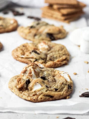 Close up of s'mores cookies loaded with marshmallows, chocolate and graham crackers on white parchment paper.