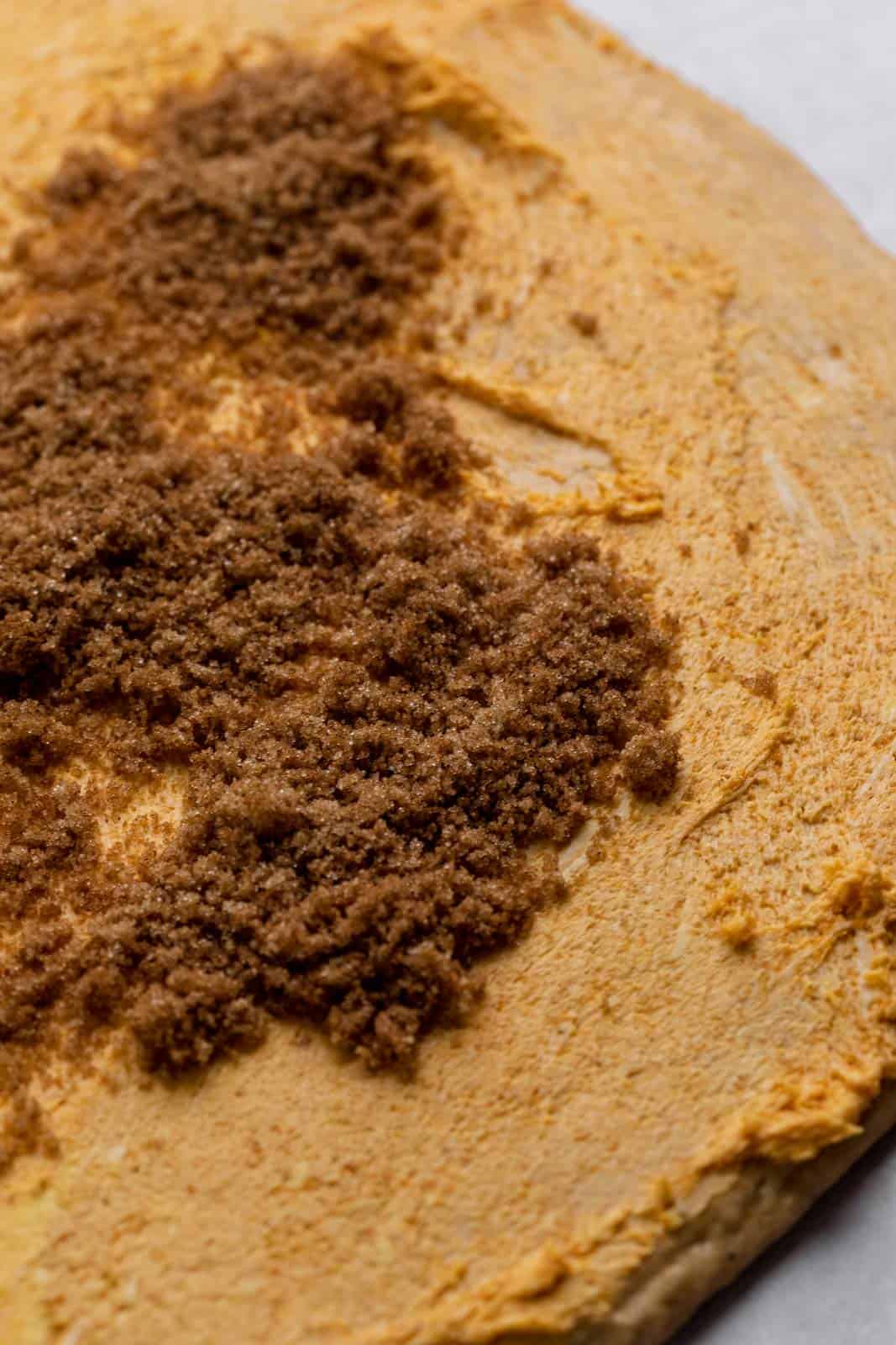 Pumpkin cinnamon roll dough spread with pumpkin butter and sprinkled with spiced brown sugar.