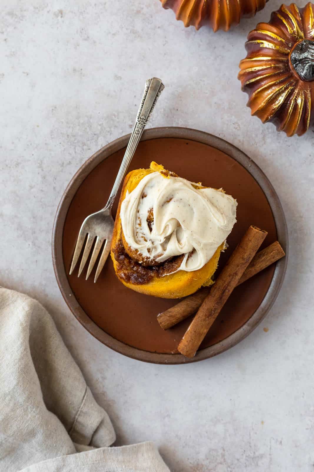 Overhead shot of a pumpkin cinnamon roll in a plate with cinnamon sticks.