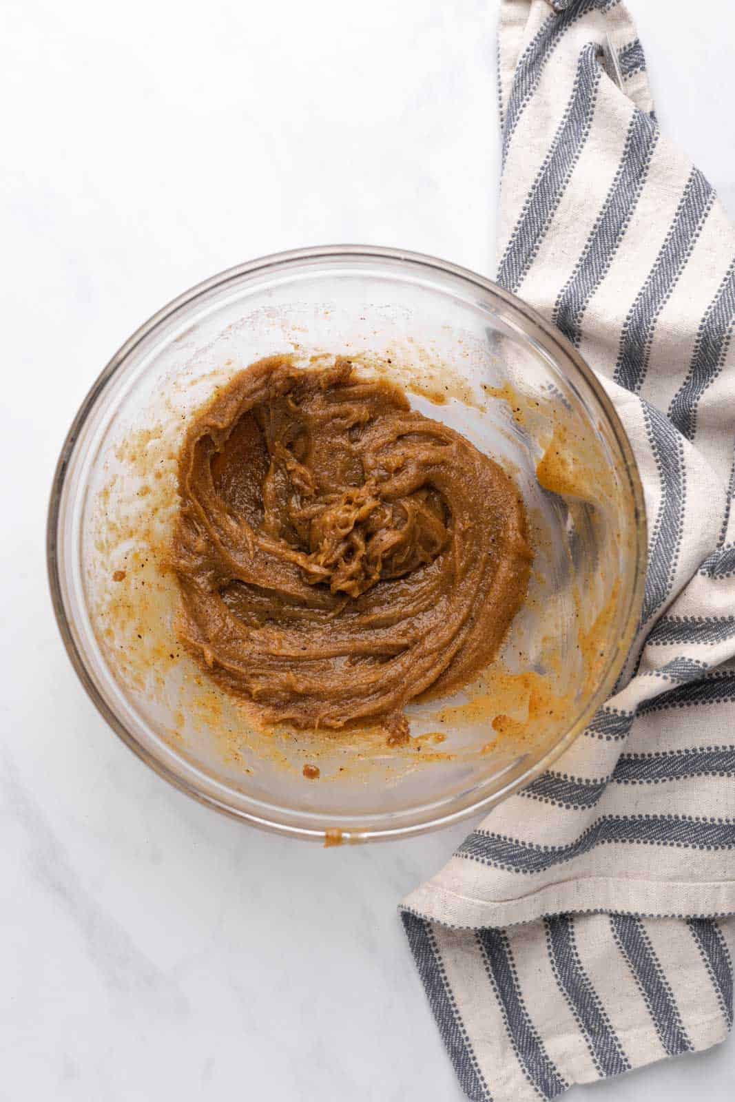 Brown butter mixed with sugar in glass mixing bowl set on a flat surface.