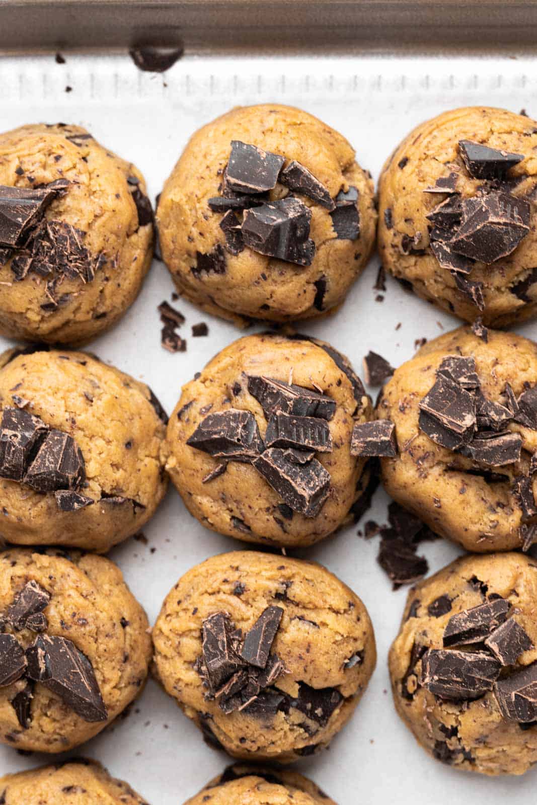 Brown butter chocolate chip cookie dough scooped into balls set on a parchment lined sheet pan.