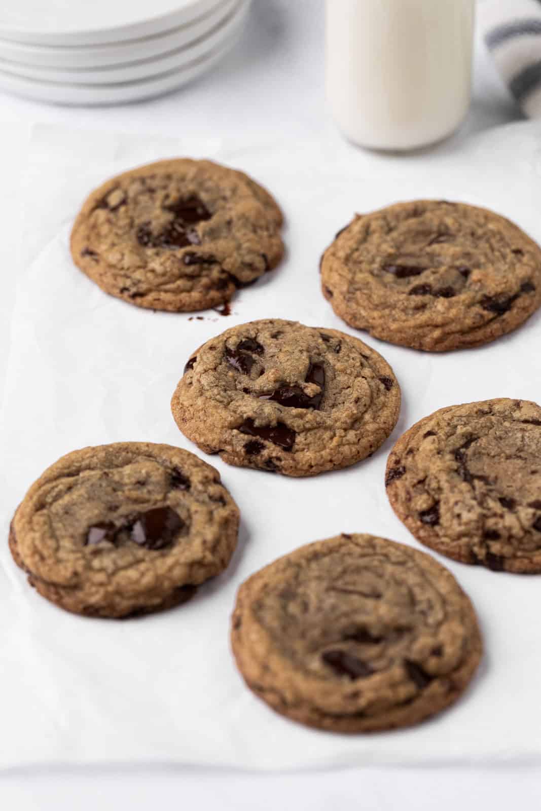 Six brown butter chocolate chip cookies arranged on parchment paper.