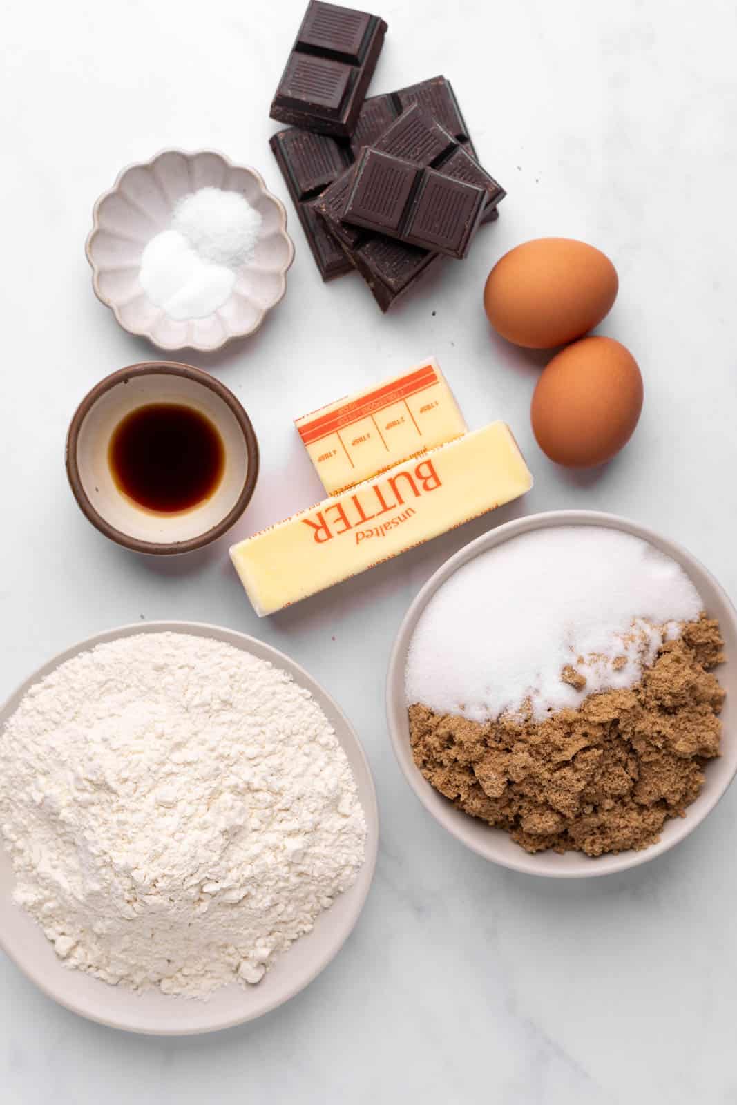 Ingredients for brown butter chocolate ship cookies set in bowls on a flat surface.
